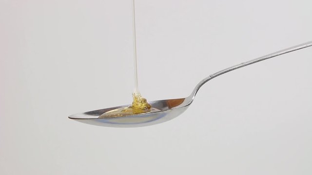 golden honey pouring onto spoon with white isolated background
