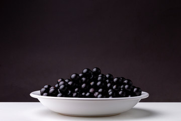 Plate with fresh shiny Jaboticaba berry fruit lit from above against a dark background