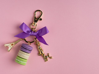 Elegant accessory key chain with golden eiffel tower and colorful macarons on pink background,...