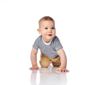 Interested infant child boy in t-shirt and green pants is crawling on all fours, looking at free copy space on white