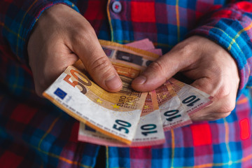 man in a red and blue plaid shirt counts money in hands. Man hands holding pile of money. pile of 10 and 50 euro banknotes in man hands