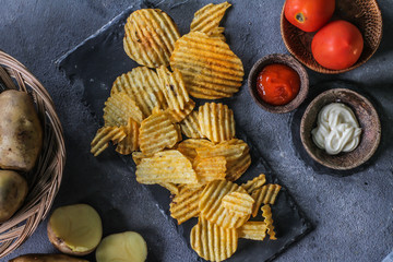 Photo of top view potato chips in a bowl on the table with ingredients around. Raw potato tomato. Salt black pepper. On a wooden table. Retro background. Studio photography. Image.