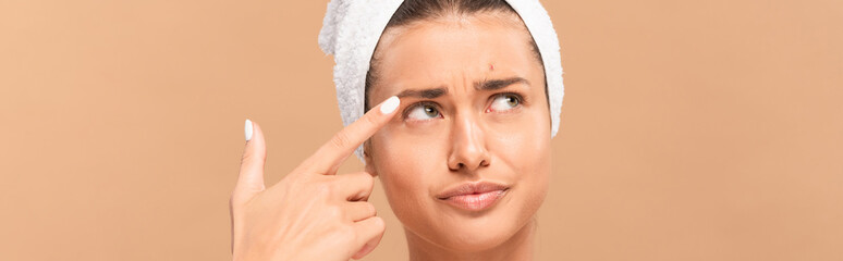 panoramic shot of displeased woman pointing with finger at face with pimple isolated on beige