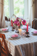 Evening dinner at home. Summer festive table setting in beautiful country house. Table decorated with pink flowers and candles.
