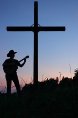 Christian religion view - silhouette of young man with hat play the guitar and sing (praise the...