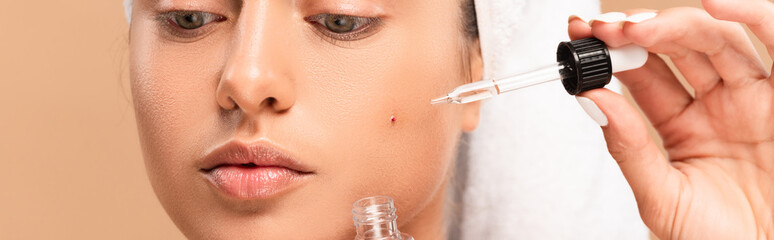 panoramic shot of woman applying serum on face with pimple isolated on beige