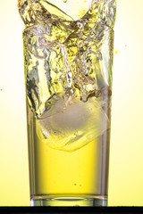 yellow carbonated lemonade in a glass with ice, flow and splash