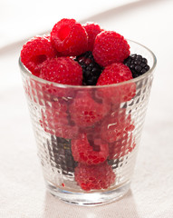 handful of fresh raspberry and blackberry berries in glass on white background