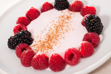 raspberries and blackberries laid out on a white plate in circle with yogurt and cinnamon