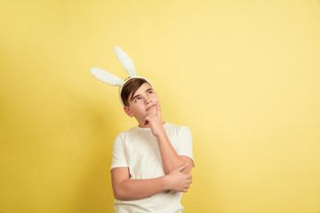 Thoughtful, dreaming. Caucasian boy as an Easter bunny on yellow studio background. Happy easter greetings. Beautiful male model. Concept of human emotions, facial expression, holidays. Copyspace.