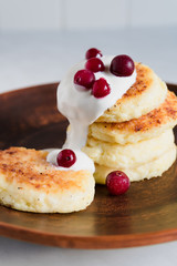 Fresh cottage cheese pancakes are stacked on top of each other and watered with sour cream and frozen cranberries.