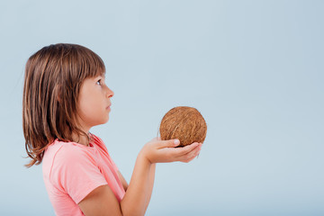 girl with coconut in hand. isolated on blue background, copy space, in studio, profile view - obrazy, fototapety, plakaty