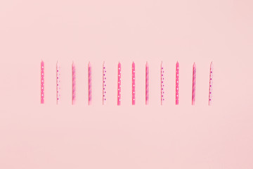 Holiday card. Pink background with scattered colored candles. Flat lay, top view.