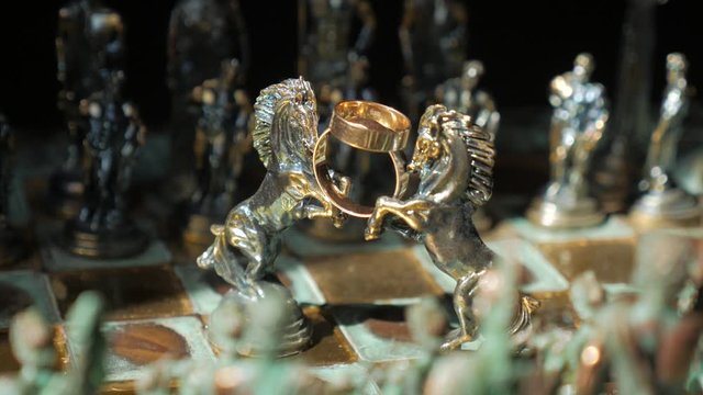Chess horses hold wedding rings on a chessboard, close-up.