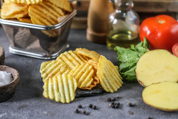 Photo of potato chips on the table with ingredients around. Raw potato tomato. Salt black pepper. On a wooden table. Retro background. On dark board. Studio photography. Image