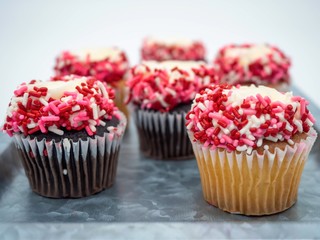 Rustic silver tray filled with chocolate and vanilla cupcakes covered in frosting, red, white and pink sprinkles taken straight on up close.  Perfect for Valentine’s Day.