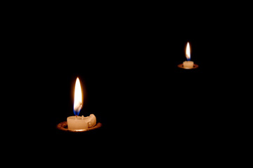 Two candles burning in the dark. The candles almost burned out. Many candles in the dark