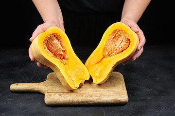 Butternut squash halves with seeds in female hands on black background, closeup. Pumpkin pieces on...