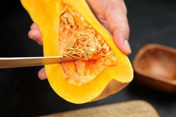 Butternut squash, Woman picks pumpkin seeds. Female hands with steel knife, wooden bowl, cutting...