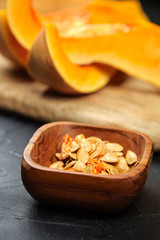 Pumpkin seeds in wooden bowl, Butternut squash pieces, cutting board on black background, closeup. Cooking winter squash