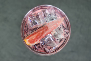 Pink gin tonic vodka soda fruit grapefruit cocktail drink in glass with ice, top view on dark background