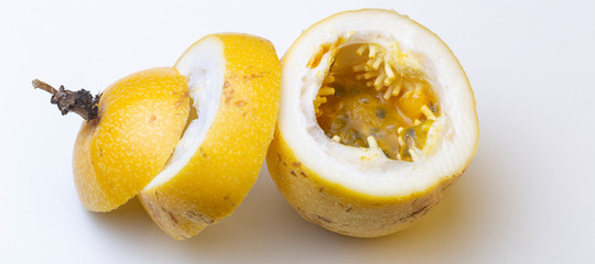 Naklejka na ściany i meble Top down view of vibrant yellow Passion fruit on a white surface with the inner structure and pulp with black seeds visible and sliced pieces of the top resting beside