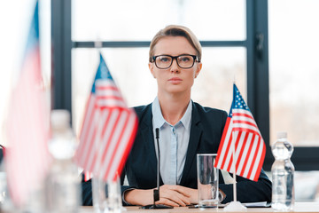 selective focus of attractive diplomat in eyeglasses near american flags on table