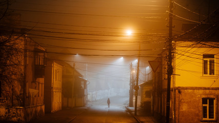 Fototapeta na wymiar Lonely woman walking in foggy old city with street lights in a coat