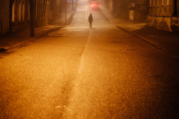 Lonely woman walking in foggy old city with street lights in a coat