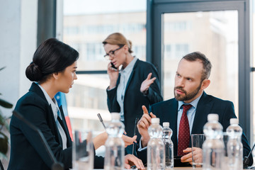 selective focus of diplomats talking and gesturing near businesswoman using smartphone