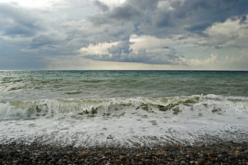Restless stormy Black Sea. The sea is stormy and the waves with white foam rush over to the pebble beach. Gloomy gray cloudy sky. A sea of various shades of green and blue