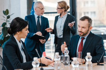 selective focus of diplomats talking and gesturing near glasses on table