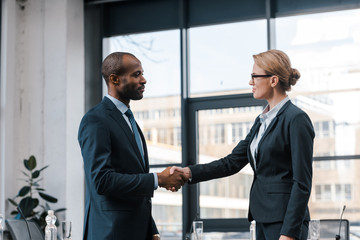 side view of attractive businesswoman shaking hands with african american businessman - obrazy, fototapety, plakaty