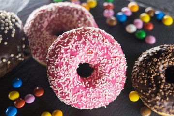 A donut in a pink glaze is spread out on a platter; chocolate colored candies lie nearby.