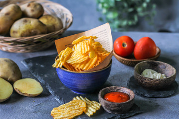 Photo of potato chips in a bowl with chili sauce on dark background. Chili ketchup. Ingredients. On a wooden table. Retro background. Front view. Studio photography. Image.