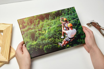 Canvas print. Photo with gallery wrap method of canvas stretching on wooden stretcher bar. Female hands hold a color travel photography (with people on zip line)