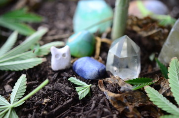 Miniature fairy garden, marijuana leaves and tiny sculptures with crystals. Healing crystals in a plant pot, cannabis leaves on display. Playful crystals and plants. Beautiful natural lighting, macro
