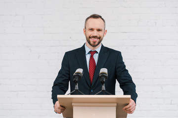 happy bearded speaker smiling near microphones and brick wall