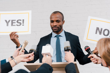 cropped view of journalists with microphones near african american diplomat holding placards with...