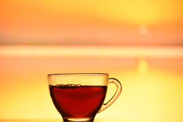 A transparent cup with black tea on the lake at sunset or dawn. Beautiful landscape in the background. an atmosphere of outdoor recreation and relaxation.