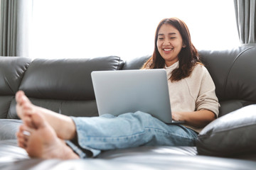 Naklejka premium Young woman doing research work for her business, Smiling woman sitting on sofa relaxing while browsing online shopping website.