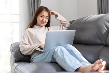 Young woman doing research work for her business, Smiling woman sitting on sofa relaxing while browsing online shopping website.