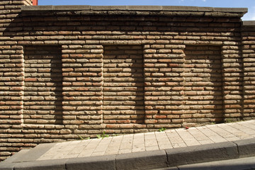 Brick wall in the old city with three grooves on the street, with a strong slope on a bright sunny day. From the dimples form small shadows. Different bricks, whole and slightly broken.Tbilisi Georgia
