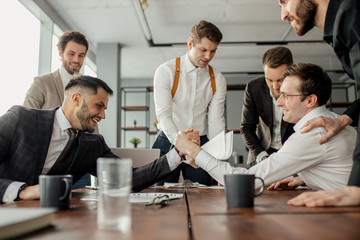 positive coworking business men in tuxedo, cheerfully playing arm wrestling after working day in office