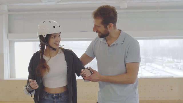 Sequence of shots of Caucasian male coach teaching young female novice rollerblader in indoor rollerdrome