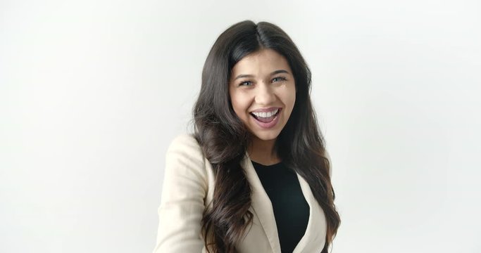 Happy attractive business lady in formal clothing laughing and pointing with forefinger on camera. Successful woman with dark hair posing in studio with white background.