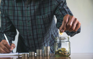 Men are saint documents about save money and put coin in glass jar on desk on black background.