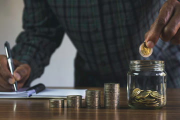 Men are saint documents about save money and put coin in glass jar on desk on black background.