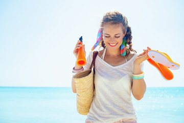 woman with straw bag, orange flip flops and bottle of sunscreen