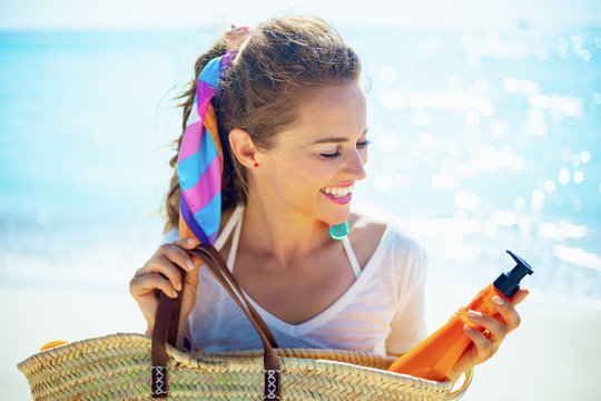 Woman On Beach Taking Orange Spf Bottle Out Of Beach Straw Bag